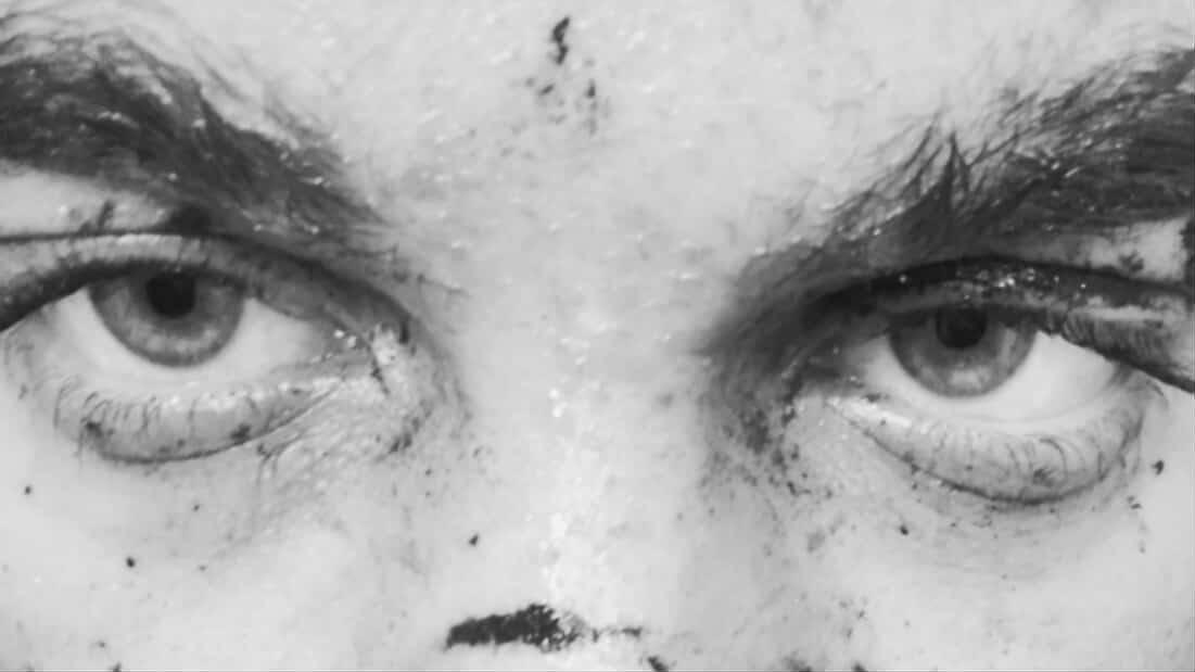 Extreme close-up black and white shot of intense human eyes staring directly into camera, skin texture visible, raw and unsettling underground visual aesthetic.